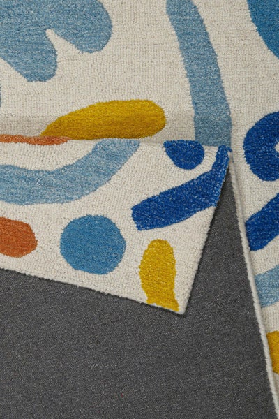 Nahaufnahme eines getufteten Teppichs mit abstrakten Mustern in Blau, Gelb und Orange. Eine Ecke ist umgeschlagen und zeigt die Rückseite.
