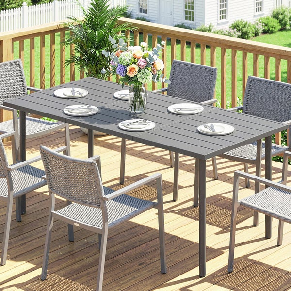 Gartenmöbel-Set aus dunkelgrauem Aluminium mit großem Esstisch und sechs Gartenstühlen auf einer Terrasse vor einem weißen Zaun.