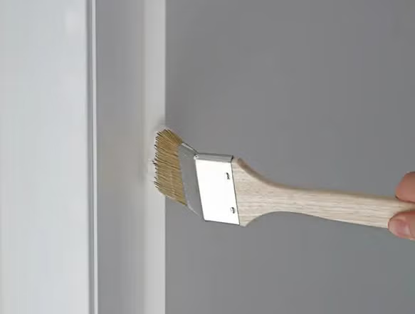 Ein abgewinkelter Heizkörperpinsel mit Holzgriff wird verwendet, um eine Wandkante präzise zu streichen.