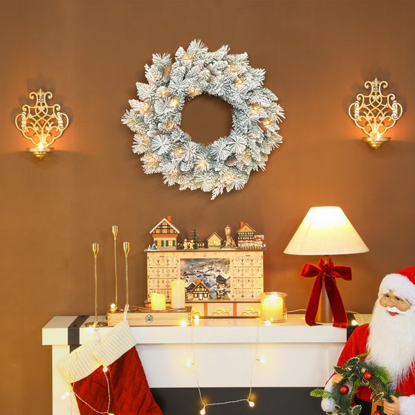 Weihnachtliche Szene mit beleuchtetem Adventskranz, hölzernem Adventskalender, Tischlampe, Kerzen und Weihnachtsmann-Figur in warmer Atmosphäre.