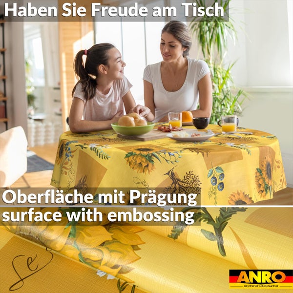 Runde Tischdecke mit Sonnenblumen-Motiv und geprägter Oberfläche auf einem gedeckten Esstisch in einem hellen Esszimmer. ANRO Logo.