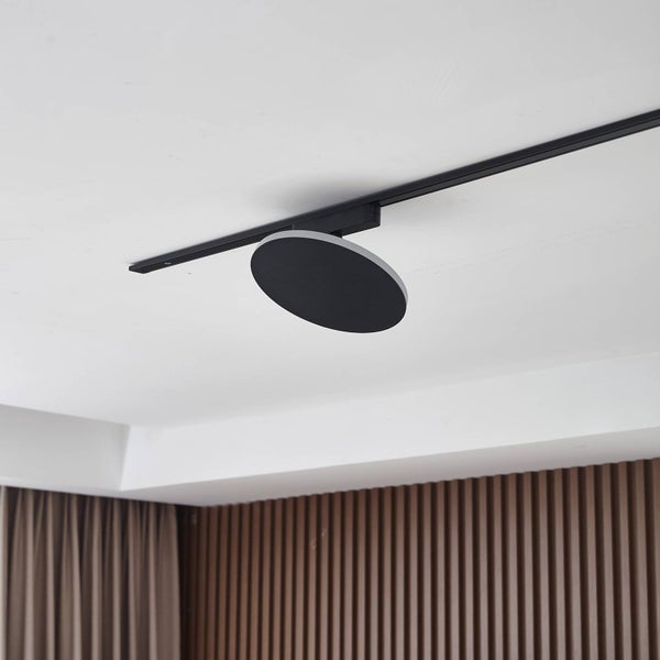 Flacher, runder Schienenstrahler in Schwarz an einer Deckenschiene in einem modernen Raum mit weißer Decke und Holzlamellenwand.