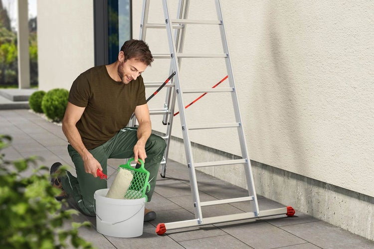 Mann beim Malern mit Farbroller, Eimer und Leiter