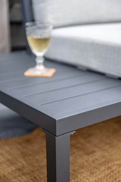 Detailaufnahme einer anthrazitfarbenen Gartenlounge aus Aluminium mit Lamellen-Abstelltisch und hellem Polster.