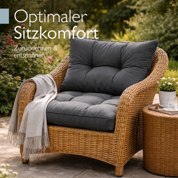 Geflochtener Gartensessel aus Polyrattan mit Polstern und Decke neben einem passenden Beistelltisch in einer hellen Gartenumgebung.