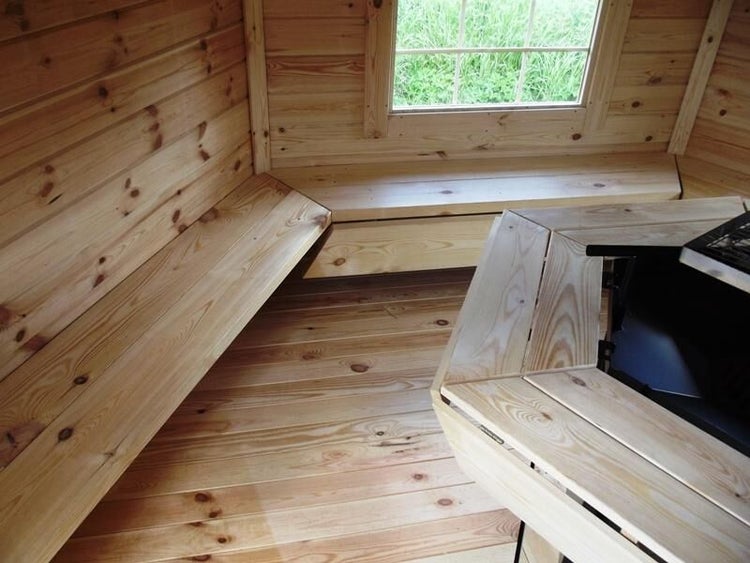 Innenansicht eines Holzhauses mit Fenster, Sitzbänken und Tisch.