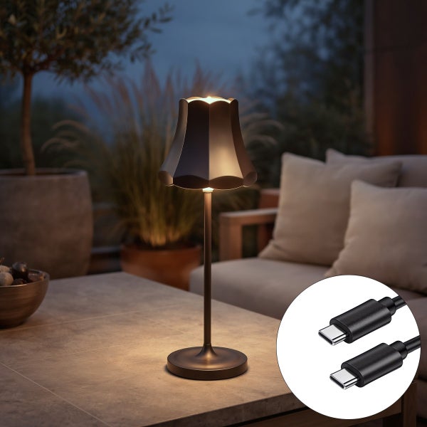 Akku LED Tischleuchte für den Außenbereich mit USB C Anschluss und Ladekabel auf einem Tisch in einer abendlichen Gartenszene.