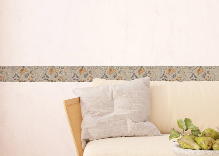 Tapetenbordüre mit botanischem Blättermuster in Erdtönen auf einer hellen Wand über einem Sofa.