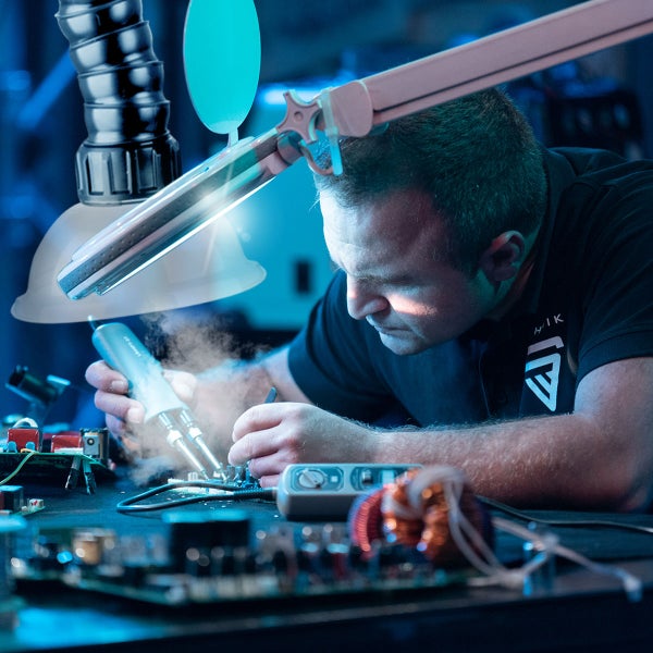 Eine Person arbeitet mit einem Lötkolben an elektronischen Bauteilen unter einer Lupenleuchte
