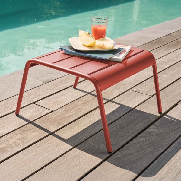 Quadratischer Gartenbeistelltisch aus Metall mit lamelierter Oberfläche auf einer Holzterrasse neben einem Swimmingpool.