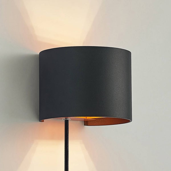 Halbrunde Wandleuchte aus Metall, außen schwarz und innen kupferfarben, mit Lichtabstrahlung nach oben und unten auf die Wand.