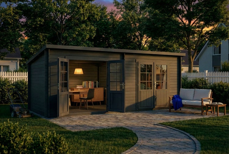 Modernes Gartenhaus aus dunkelgrauem Holz mit Pultdach, eingerichtet als Büro, auf einer Steinterrasse in einem Garten bei Dämmerung.