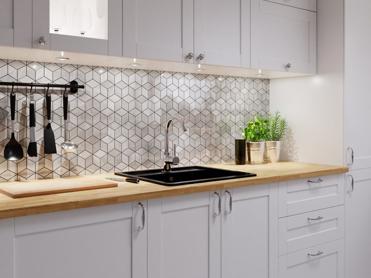 Helle Küche mit Arbeitsplatte aus Holz, schwarzem Spülbecken und Fliesenspiegel mit Hexagon-Fliesen in Marmoroptik.