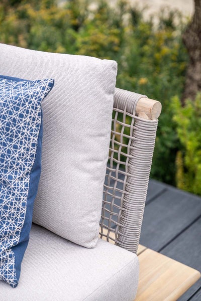 Detailaufnahme eines Garten-Loungesofas mit Holzrahmen, Seilbespannung, dicken Polstern und einem gemusterten Dekokissen.