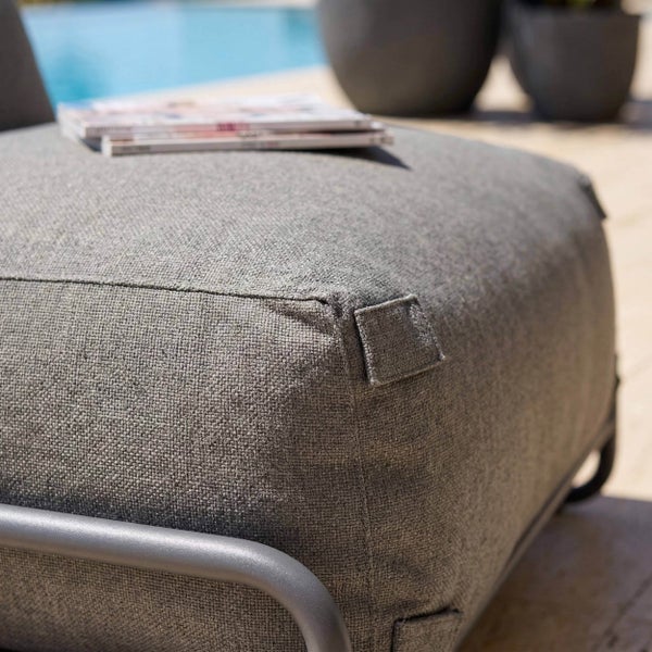 Grauer Outdoor-Hocker mit strukturiertem Stoff und Metallrahmen in einem hellen Außenbereich am Pool.