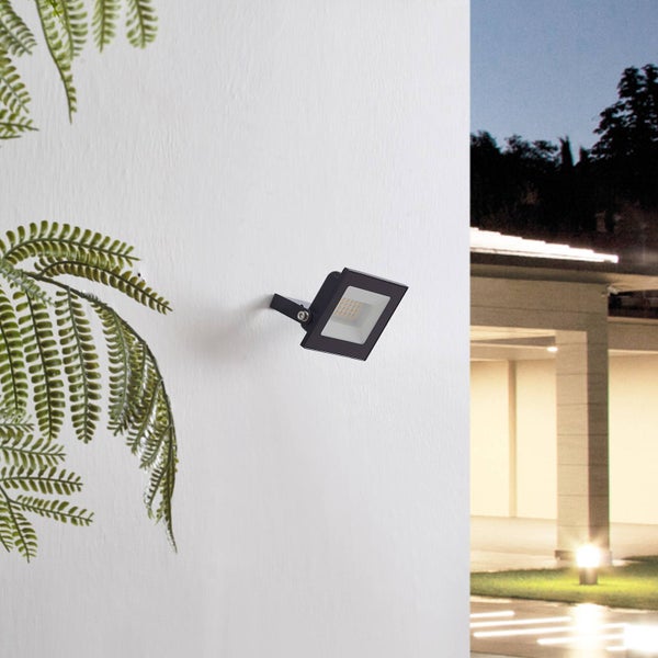 Schwarzer LED Außenstrahler an einer weißen Wand montiert, im Hintergrund ein beleuchteter Carport bei Nacht.