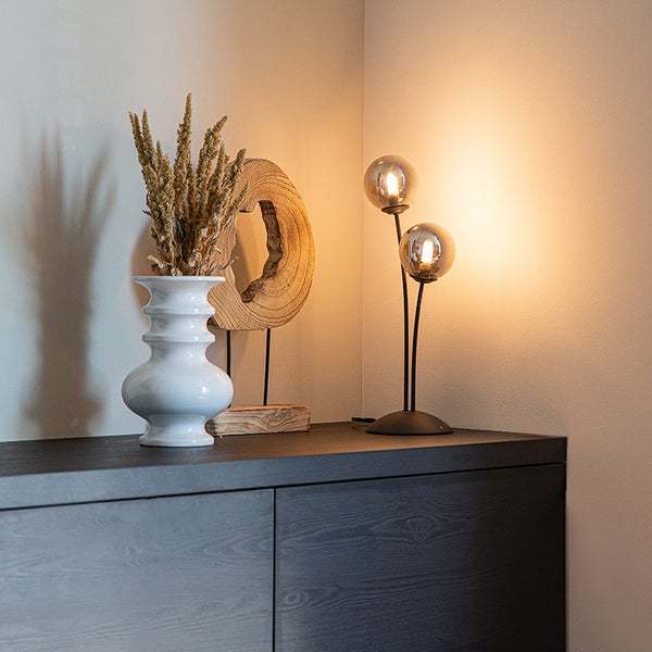 Dekoratives Arrangement mit Lampe, Vase und Holzobjekt auf einer Kommode