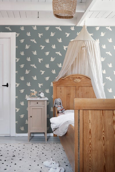 Hell eingerichtetes Kinderzimmer mit Holzbett, Nachttisch und Tapete mit Vogelmuster