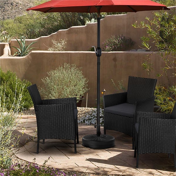 Schwarzer Sonnenschirmständer aus Kunststoff mit drei schwarzen Geflechtstühlen auf einer Steinterrasse im hellen Garten.