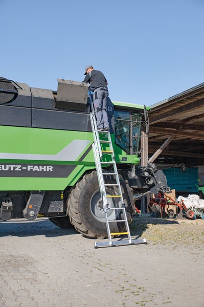 Mann auf einer Aluminiumleiter, die an einer landwirtschaftlichen Maschine lehnt