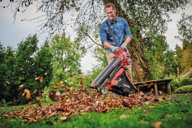 Ein Mann benutzt einen akkubetriebenen Laubsauger und Laubbläser von Einhell, um Blätter im Garten zu entfernen.