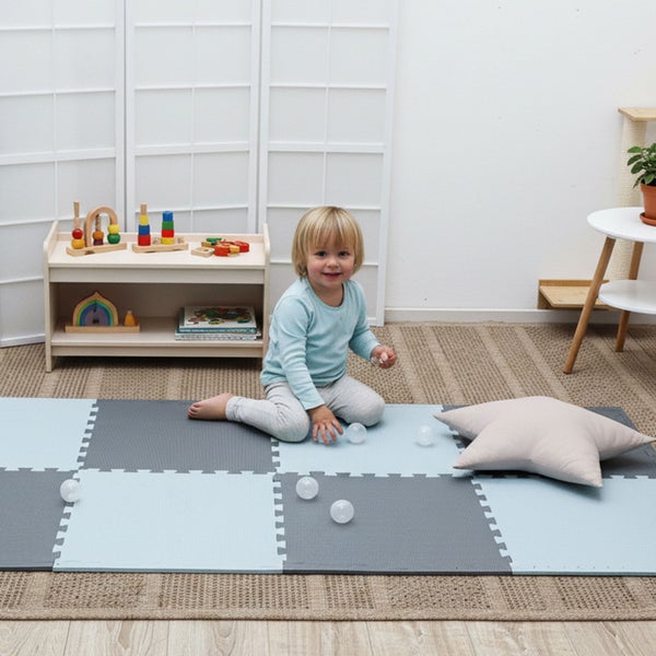 Kleinkind spielt auf Puzzlespielmatten aus Schaumstoff in einem hellen Kinderzimmer mit Holzregal und sternförmigem Kissen.