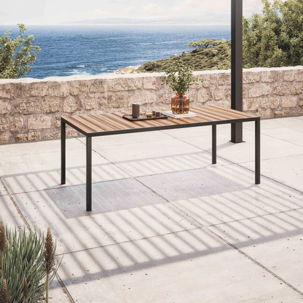 Rechteckiger Gartentisch mit Holzlamellen und dunklem Metallgestell auf einer Terrasse mit Steinmauer und Meerblick.