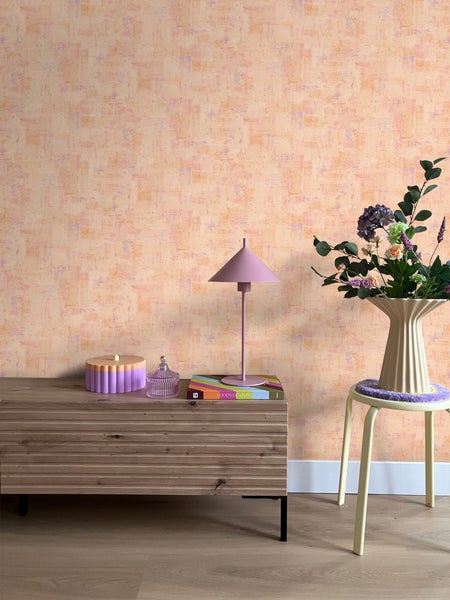 Wohnraum mit gemusterter Tapete, Kommode, Lampe, Blumenstrauß und Hocker