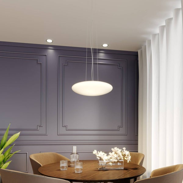 Moderne flache Pendelleuchte über einem runden Holztisch in einem hellen Esszimmer mit dekorativen Wandpaneelen und Vorhängen.