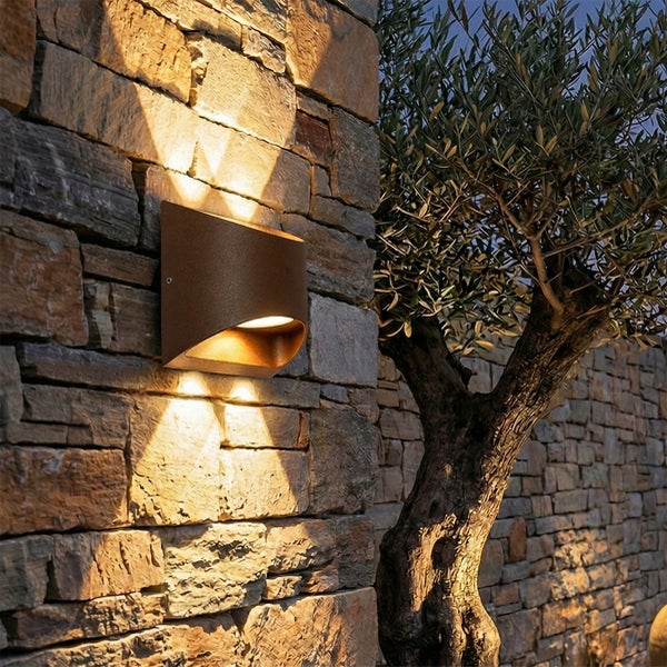 Außenwandleuchte mit Up-and-Down-Lichteffekt an einer strukturierten Natursteinwand im Garten neben einem Baum.