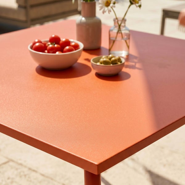 Moderner Gartentisch mit orangefarbener Oberfläche, Snackschalen und Blumenvasen auf einer hellen Terrasse.