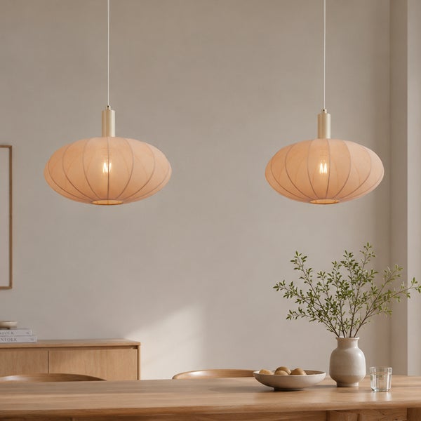 Zwei moderne Pendelleuchten mit ovalem Stoffschirm über einem Holzesstisch in einem hellen, wohnlichen Esszimmer mit einer Vase als Dekoration.