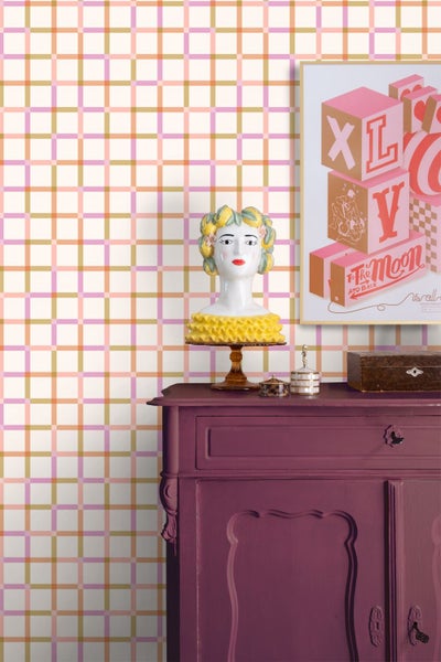 Vliestapete mit buntem Karomuster auf einer Wand hinter einer violetten Kommode mit dekorativen Gegenständen.