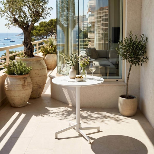 Moderner runder Bistrotisch in Weiß auf einem sonnigen Balkon mit mediterraner Dekoration und Meerblick.