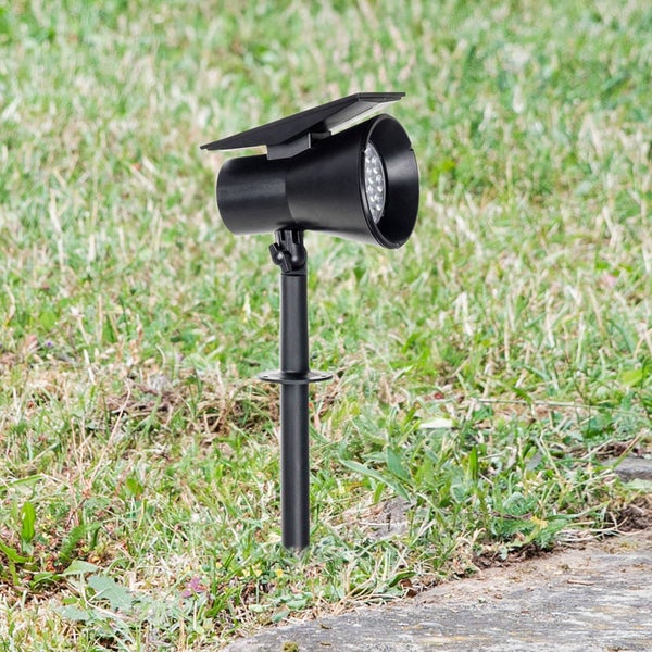 Schwarzer Solar-Gartenstrahler mit Erdspieß und integriertem Solarpanel auf einer Rasenfläche neben einem Steinweg.