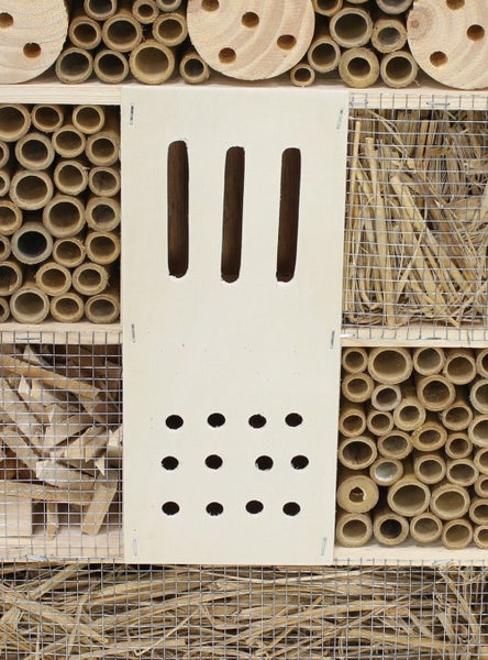 Insektenhotel mit verschiedenen Nistmaterialien wie Bambusröhren, gebohrtem Holz und Stroh sowie einer Frontplatte mit Einflugschlitzen.
