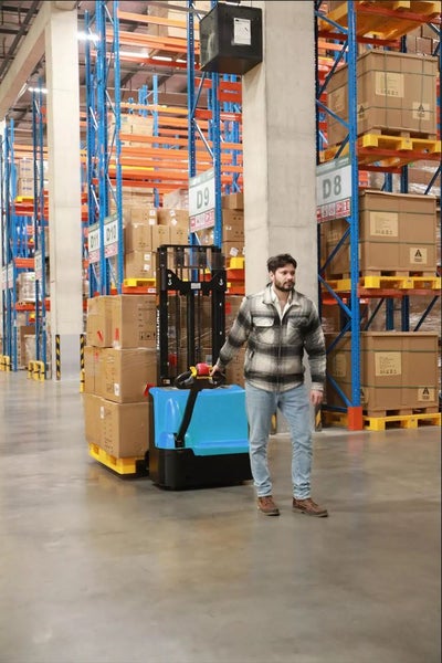 Ein Arbeiter bedient einen Gabelhubwagen in einem Lagerhaus mit Regalen.