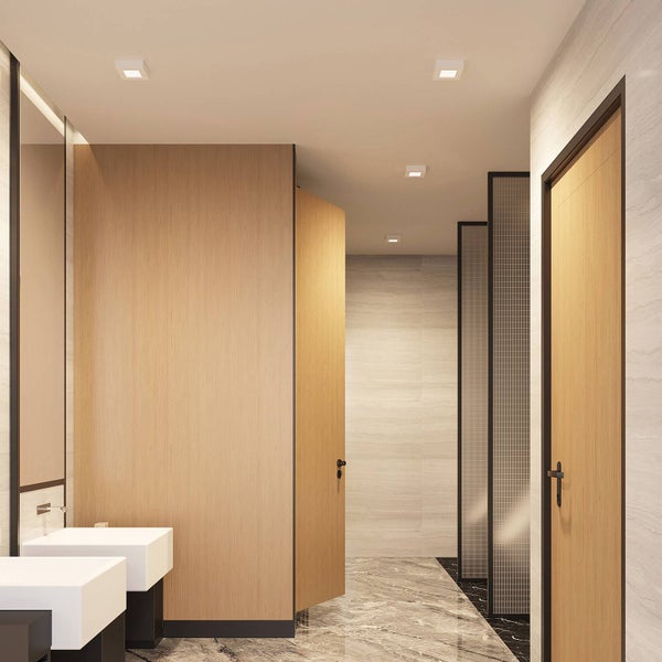 Moderner Sanitärraum mit Toilettenkabinen aus Holz, weißen Waschbecken, Marmorfußboden und quadratischen LED-Einbauleuchten in hellem Design.