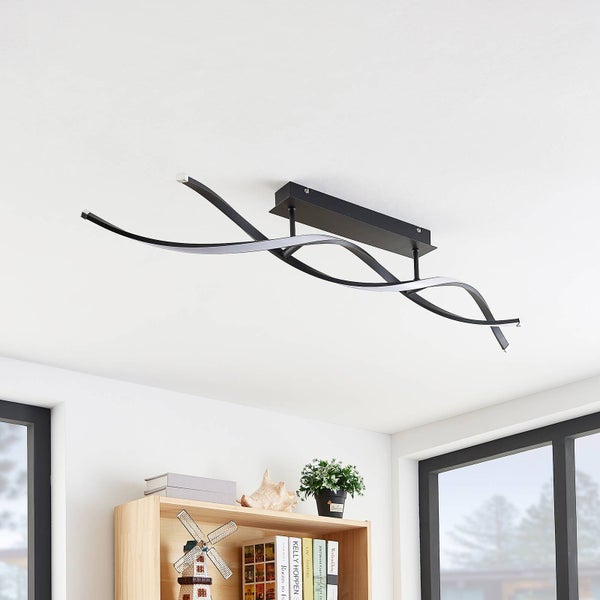 Moderne LED-Deckenleuchte mit geschwungenen schwarzen und weißen Metallarmen in einem hellen Raum über einem Holzregal.