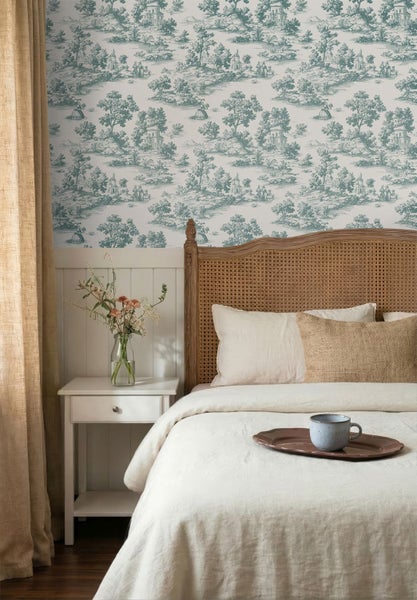 Helles Schlafzimmer mit Toile-de-Jouy-Tapete, weißen Wandpaneelen, Bett mit Wiener Geflecht, weißem Nachttisch und Leinenvorhängen.