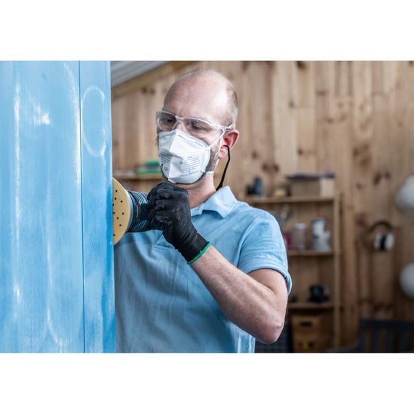 Handwerker schleift eine blaue Holzoberfläche mit einer Schleifmaschine, Schutzbrille, Mundschutz und Handschuhen