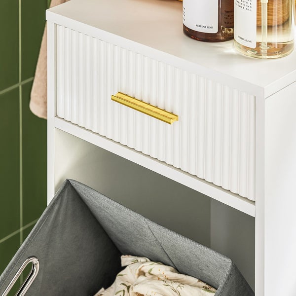 Detailaufnahme eines weißen Badezimmerschranks mit Schublade, goldenem Griff und Wäschekorb