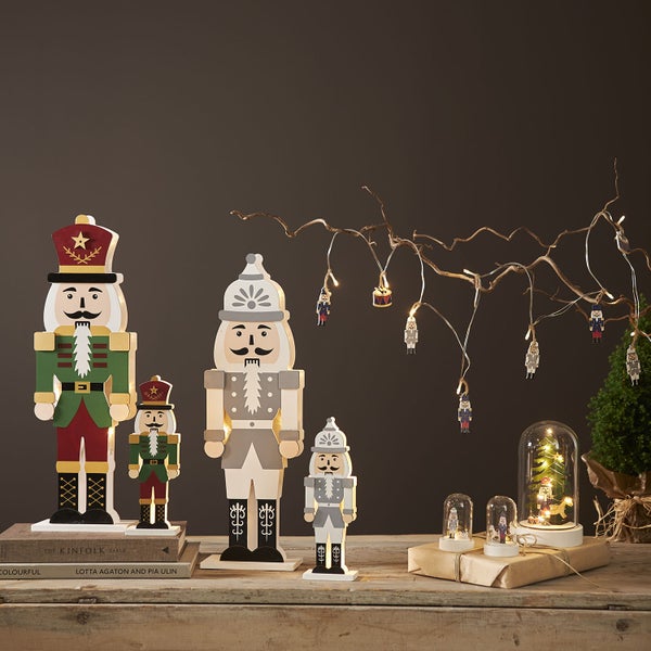 Dekorative Szene mit Nussknackern aus Holz und beleuchteten Weihnachtskugeln unter Glasglocken