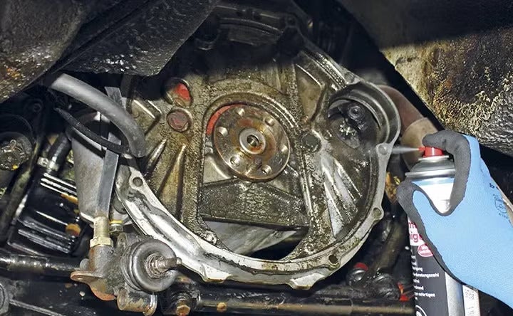 Reinigung eines verschmutzten Bauteils am Fahrzeug mit einem Sprühreiniger.