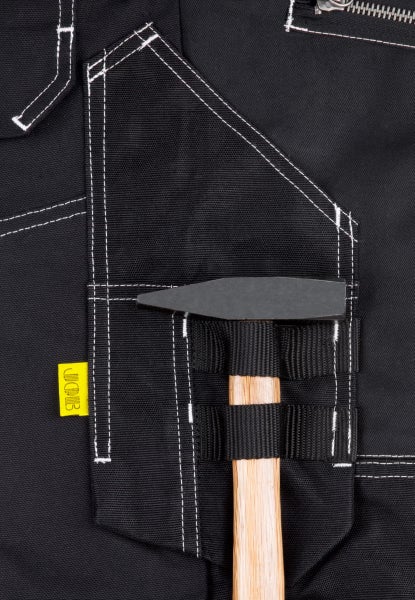 Nahaufnahme einer schwarzen Arbeitshose mit JCB Logo, weißer Kontrastnaht und einer Hammerschlaufe, in der ein Hammer steckt.