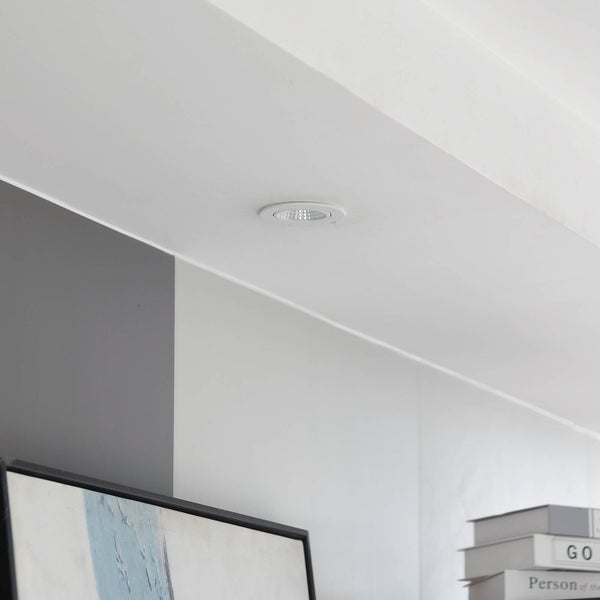 Runder weißer LED Einbaustrahler in einer hellen Decke montiert, modernes Interieur mit grauer Wand und Dekoration.