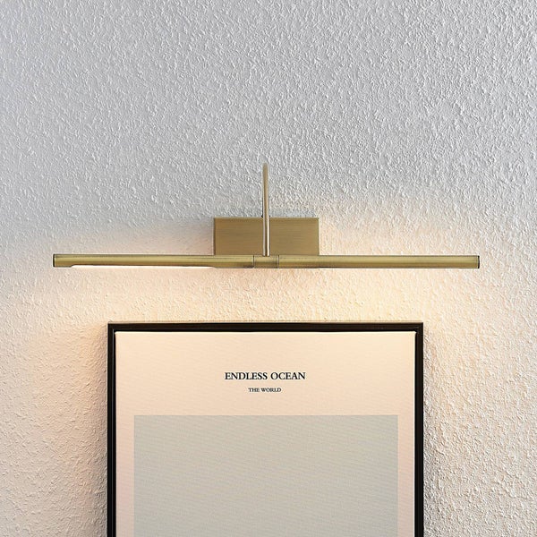 Lineare Bilderleuchte aus Metall in Messingoptik montiert über einem gerahmten Bild an einer strukturierten Wand.