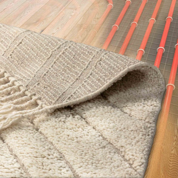 Fußbodenheizung unter einem Holzfußboden mit einem zurückgeschlagenen, hellen strukturierten Teppich.