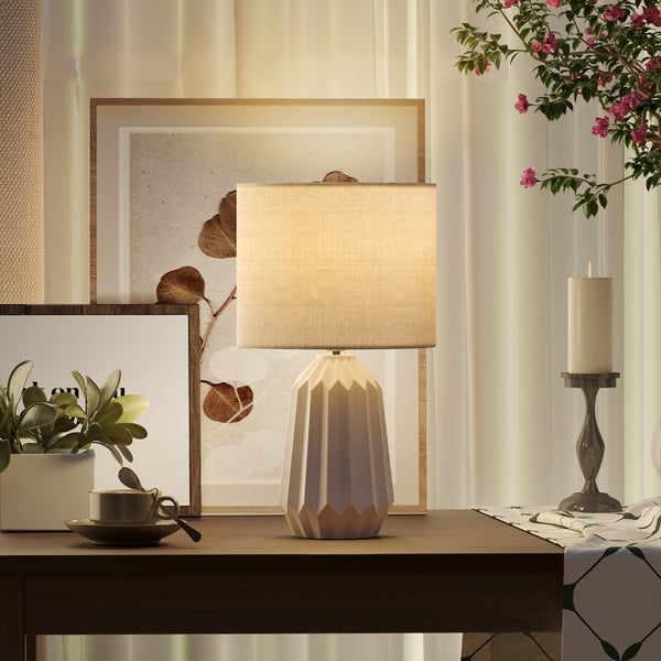 Dekorative Tischleuchte mit geometrischem Sockel und Stoffschirm auf einem Nachttisch