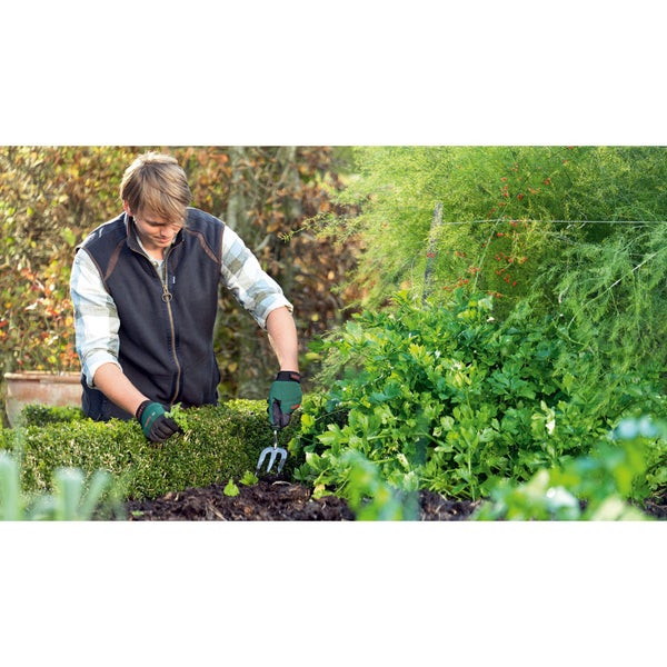 Eine Person arbeitet mit einer Gartenkralle und Handschuhen im Garten.